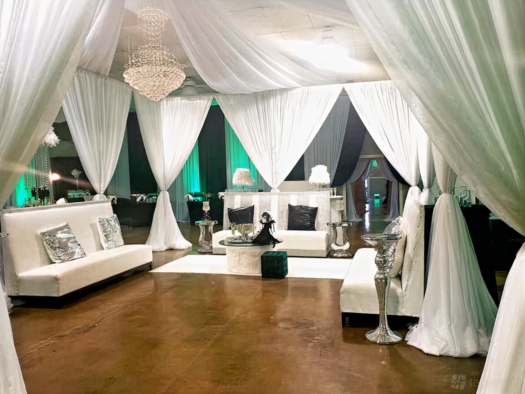 An event venue with white draped curtains, chandeliers, plush seating, and silver accent tables at Unique Visions Upscale Events.