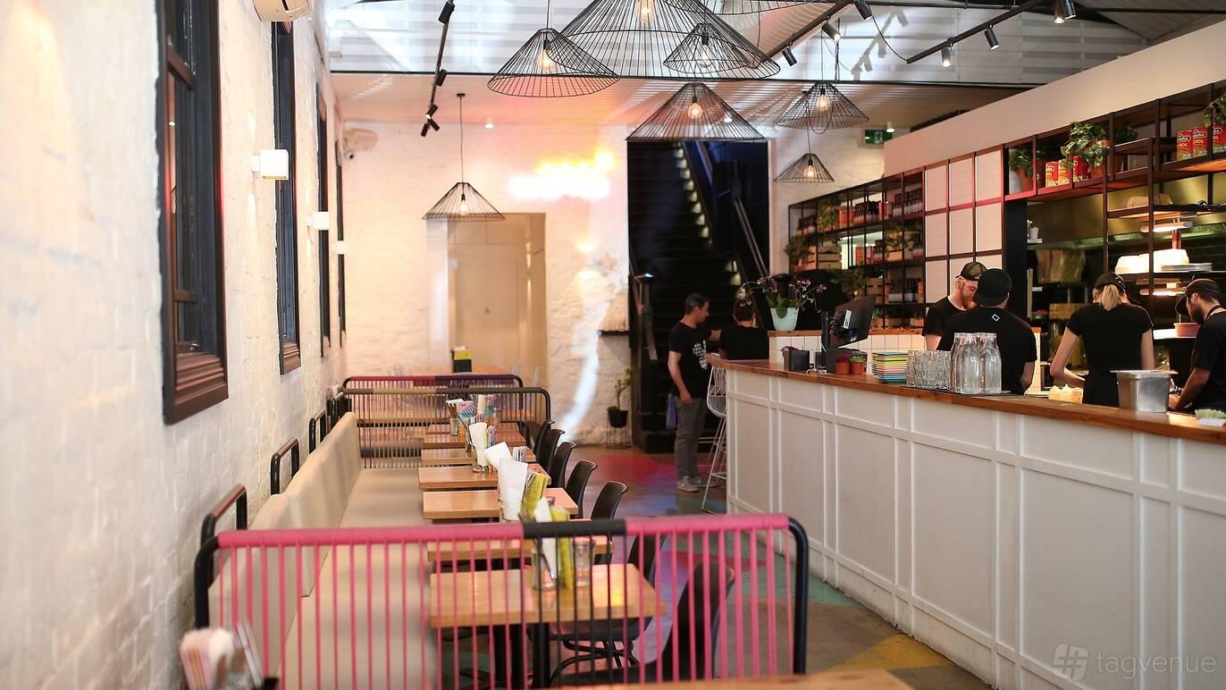 An event space in a restaurant with long wooden tables, pink railings, and pendant lighting at Fonda Mexican @ Windsor.