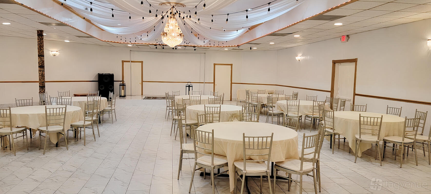 A banquet hall with round tables draped in white linens, chiavari chairs, and draped ceiling with string lights at Lazeeza Grill Restaurant & Banquet Hall.