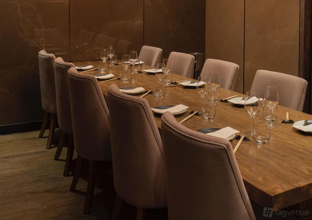 A dining room with a long wooden table set with glassware and neutral upholstered chairs at Muni Robata.