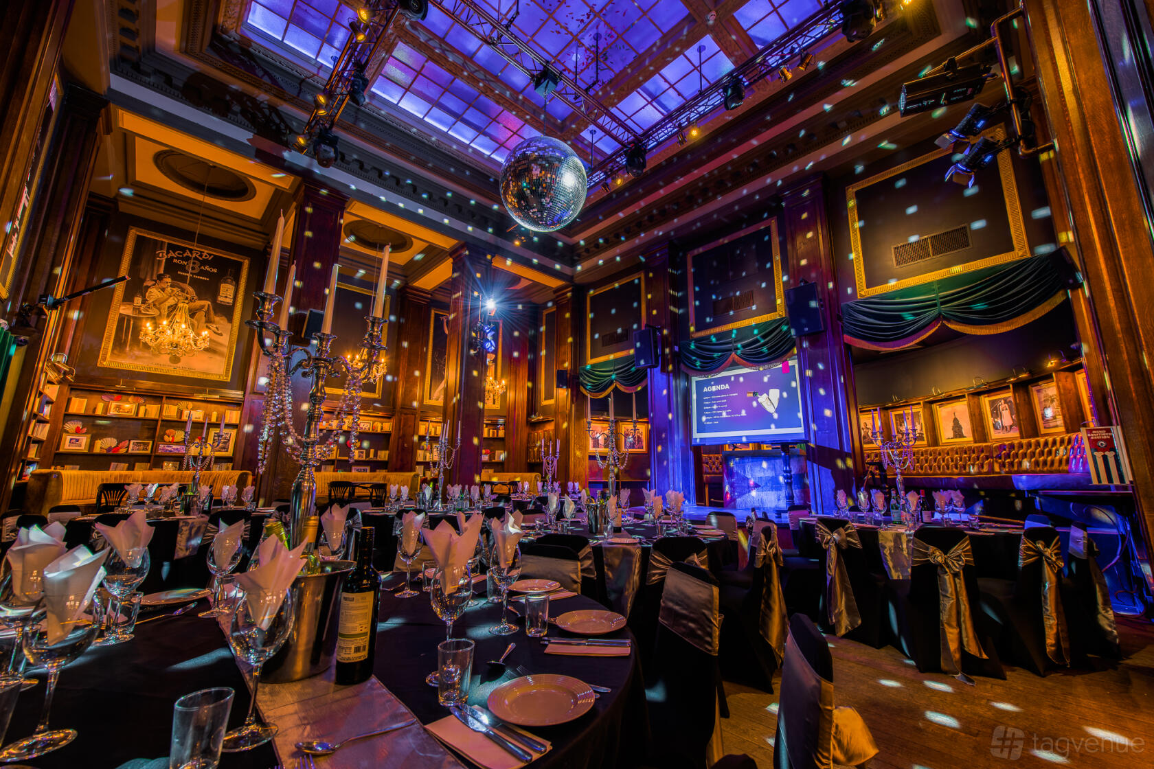 A function room with round tables, black chair covers, a disco ball, and spotlights at Revolucion De Cuba Birmingham.
