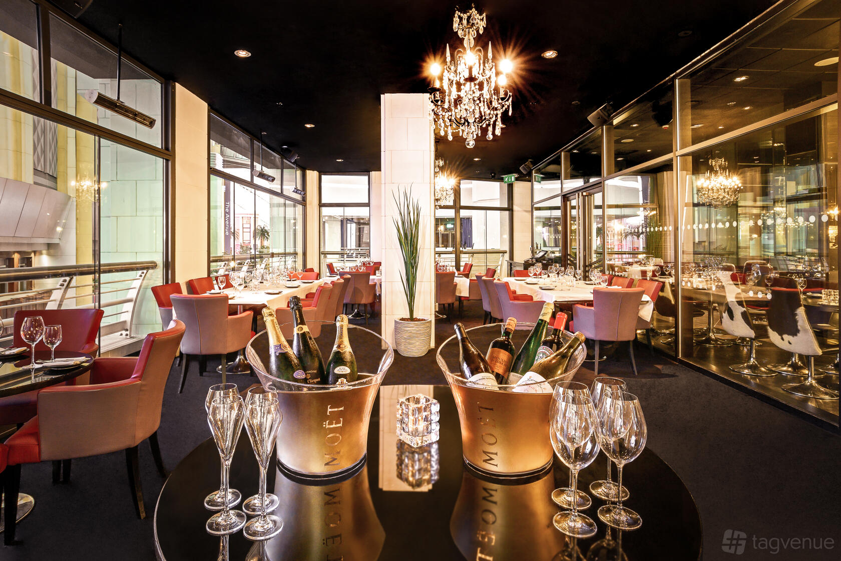 A restaurant dining room with floor-to-ceiling windows, chandeliers, and tables set with glassware at Gaucho O2 Arena.