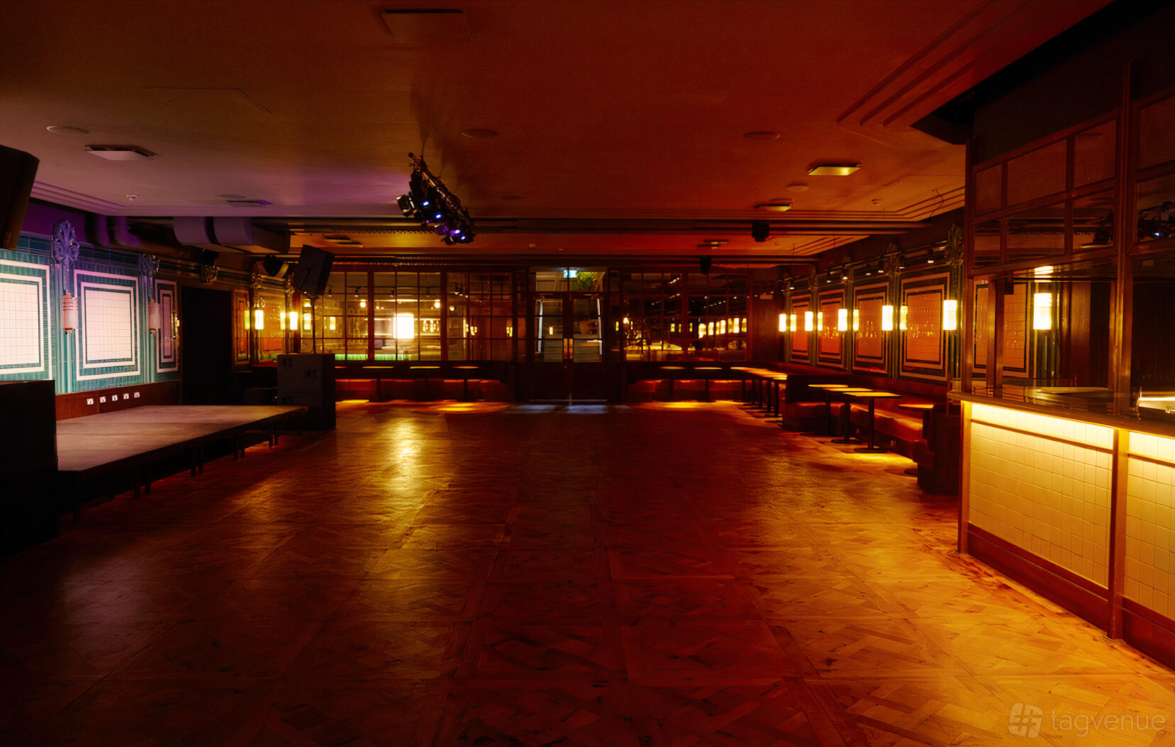 A ballroom with wood parquet flooring, stage, mirrored walls, and warm wall lighting at Oneninetyfour.