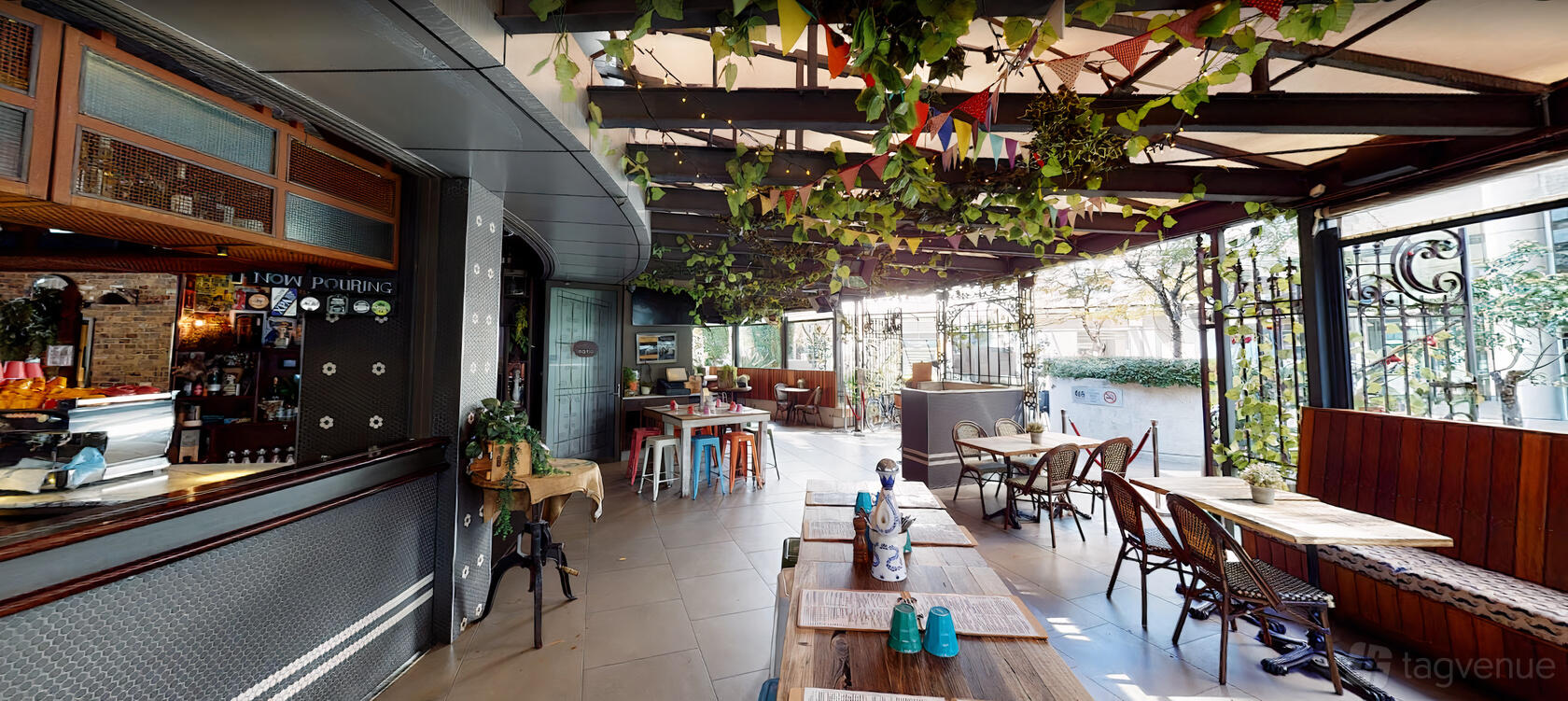 A restaurant terrace with wooden tables, rattan chairs, hanging foliage, and colorful pennant banners at 465 The Avenue.