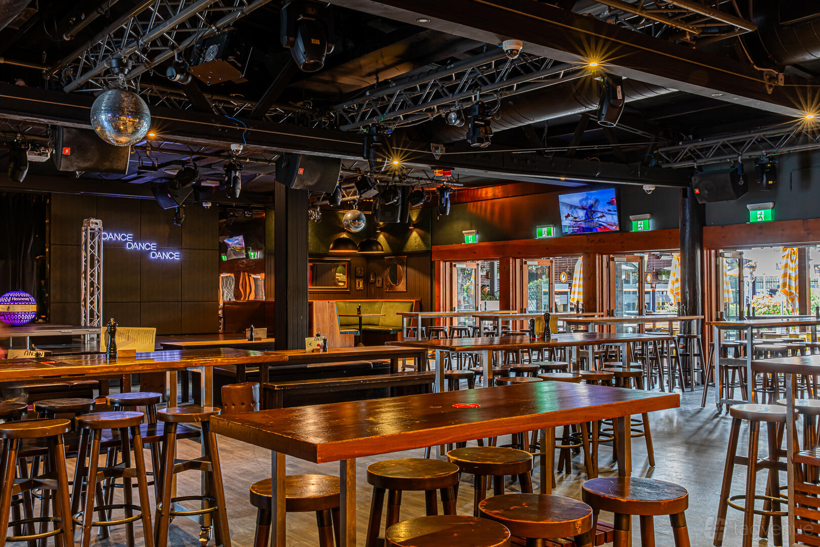 A pub lounge with wooden high tables, bar stools, stage lighting, and neon signage at Albion Hotel.