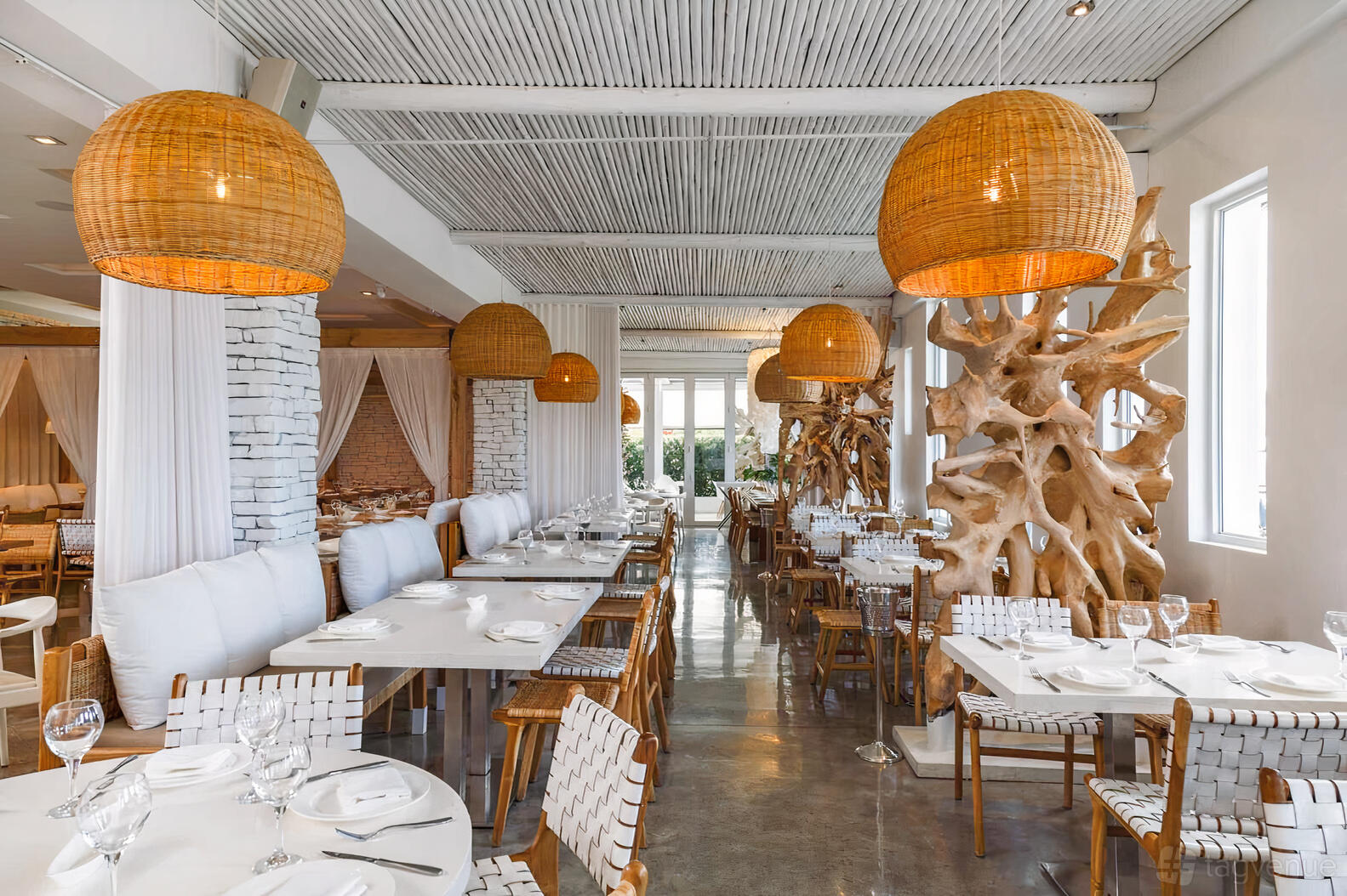 An event space in a restaurant with woven pendant lights, white brick columns, and wooden seating at Thasos.