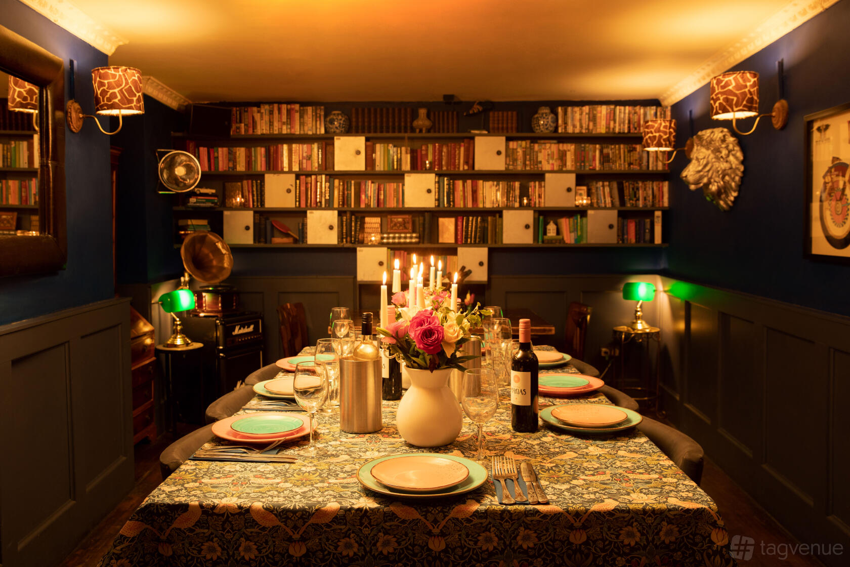 An event space in a cocktail bar with bookshelves, candelabra lighting, and a floral tablecloth at The Little Blue Door.