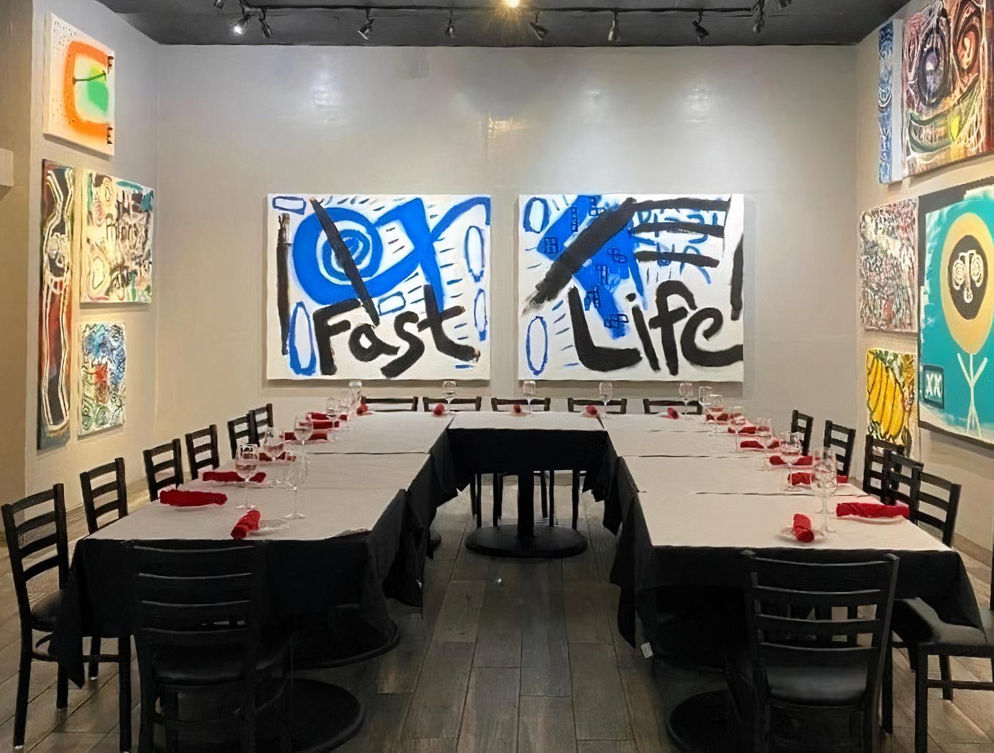 A dining room with U-shaped table setup, black chairs, white linens, and colorful modern art at Pizzeria Vivoli & Italian Grill.