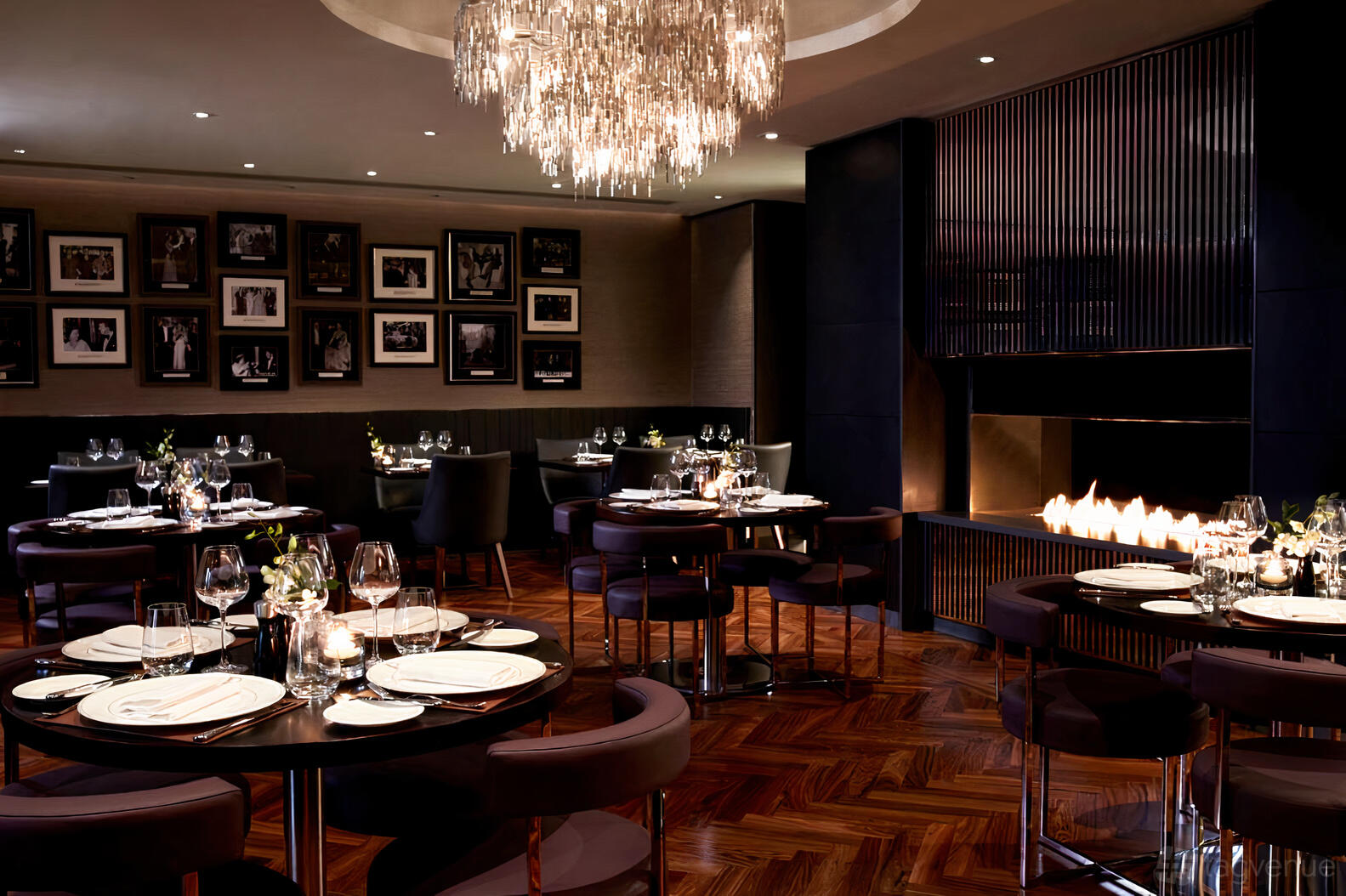 A cocktail bar with round tables set for dining, a modern fireplace, and a crystal chandelier at POTUS Bar & Restaurant.