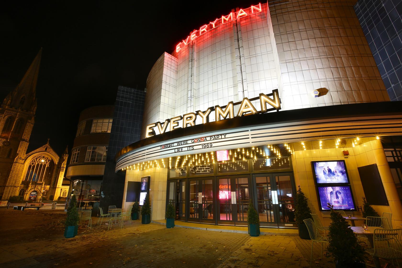 A cinema with curved art deco facade, illuminated signage, and outdoor seating at Everyman Muswell Hill.