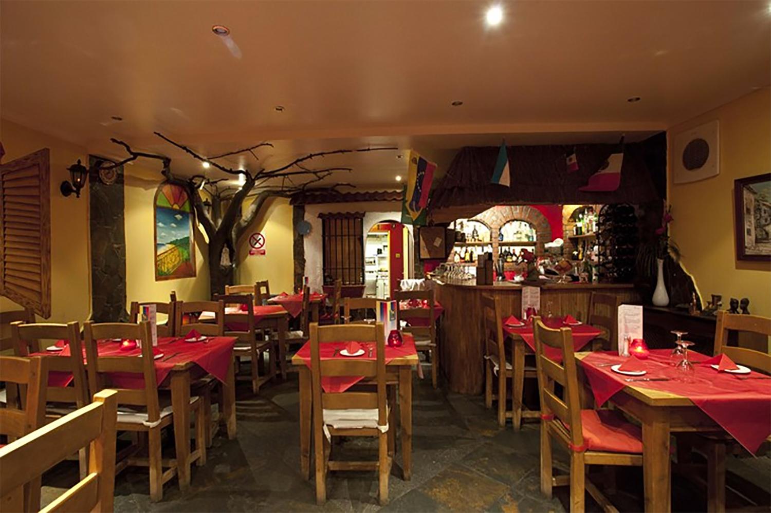A dining room with wooden tables, red tablecloths, and decorative tree branches at Sabor Criollo.