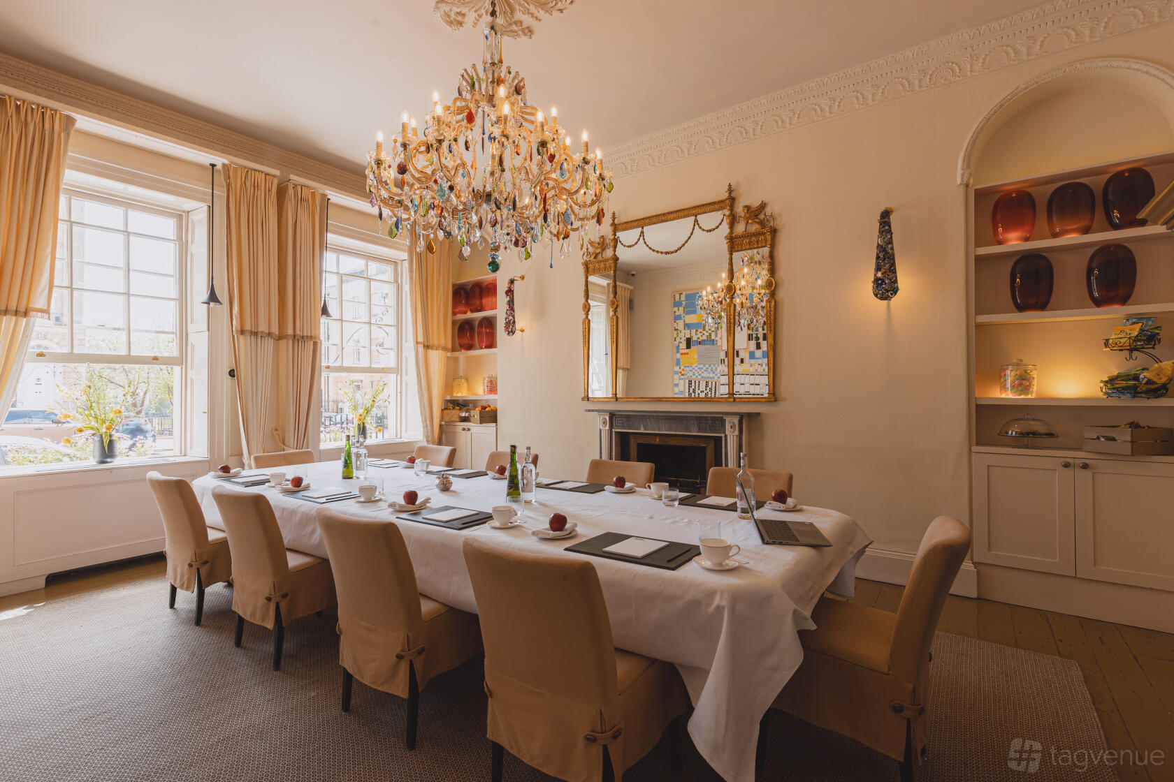 A hotel function room with a long table set for a meeting, chandelier, large windows, and ornate mirror at No.15 by GuestHouse, Bath.