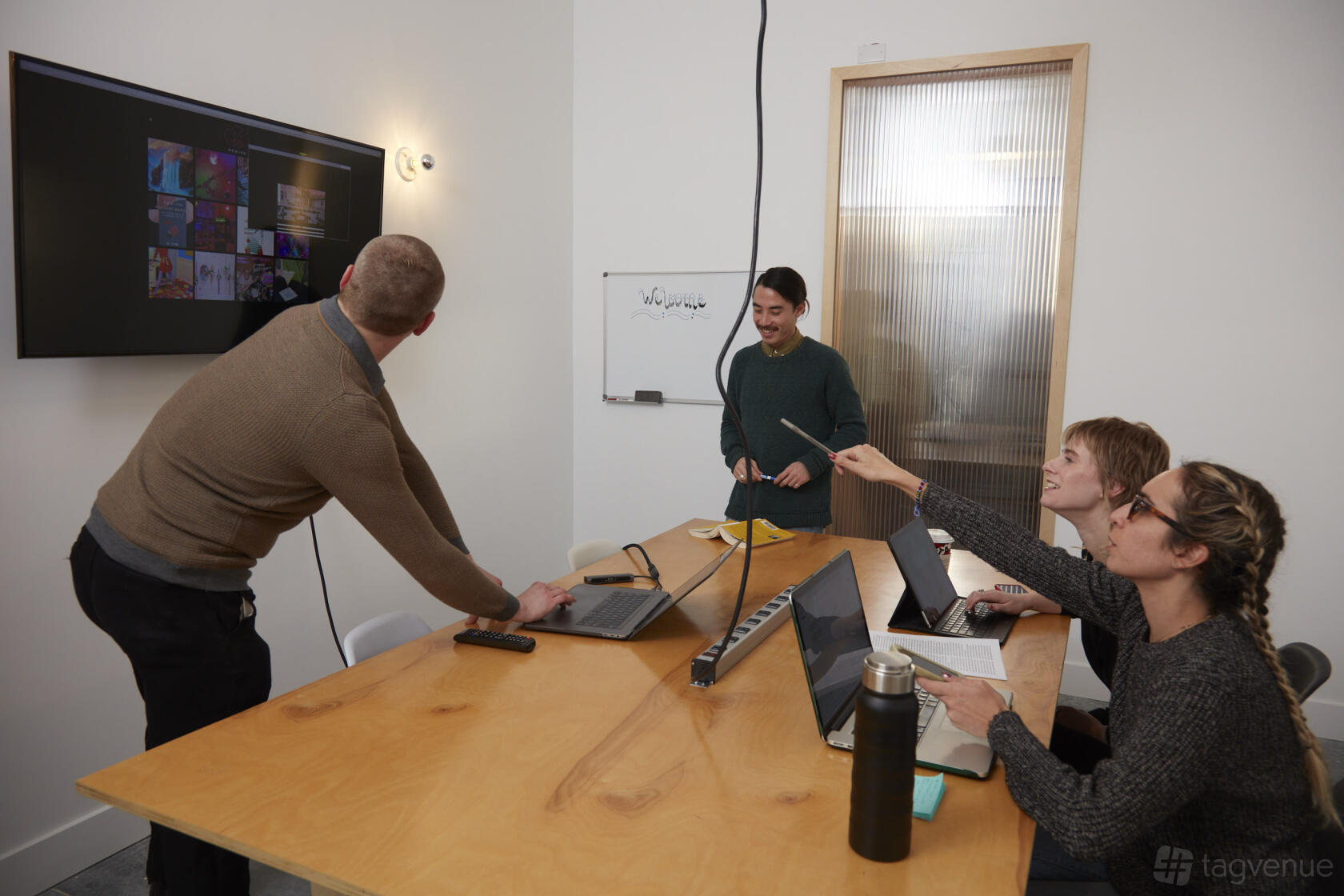 A meeting room with a wooden table, wall-mounted screen, laptops, and a small whiteboard at Hunters Point Studios.
