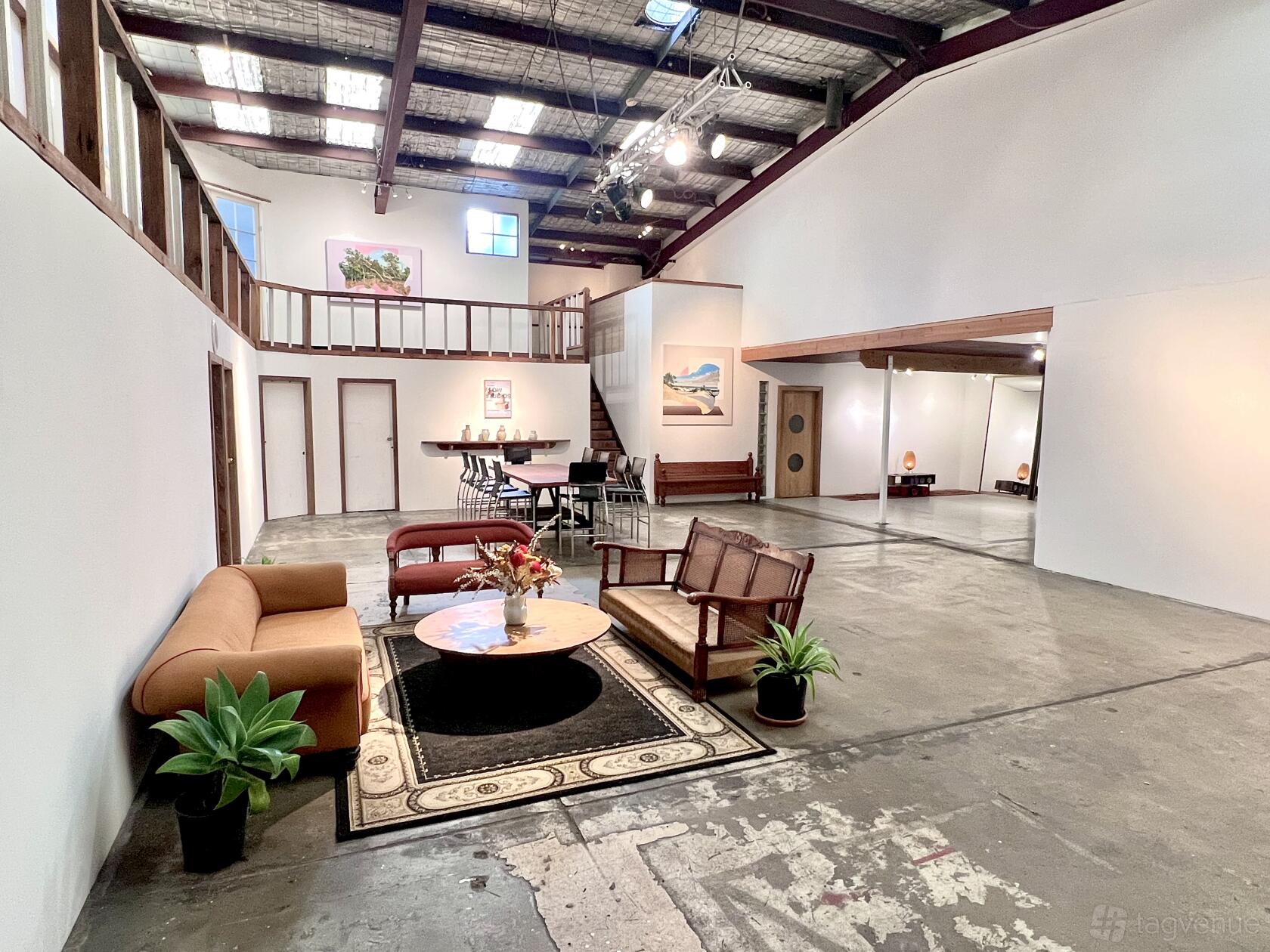 A gallery with exposed beam ceilings, white walls, and lounge seating on a patterned rug at Flow Studios.