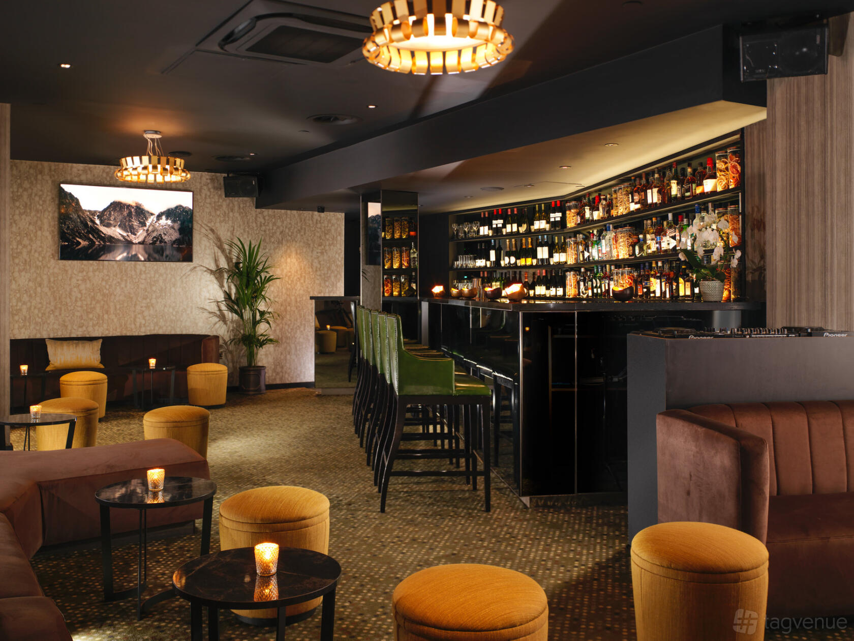 An event space in a hotel with a stocked bar, velvet barstools, plush seating, and warm lighting at St Martins Lane London.
