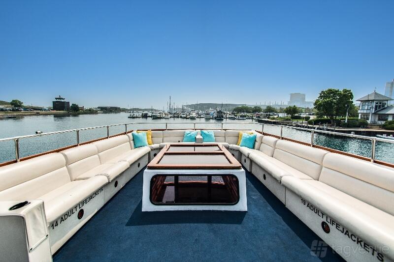 A yacht deck with built-in cushioned seating, throw pillows, and marina views at Sophisticated Lady Yacht Charters.