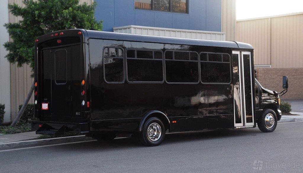 A black party bus with tinted windows and chrome wheels parked outside Abbie Party Bus and Limo Service.