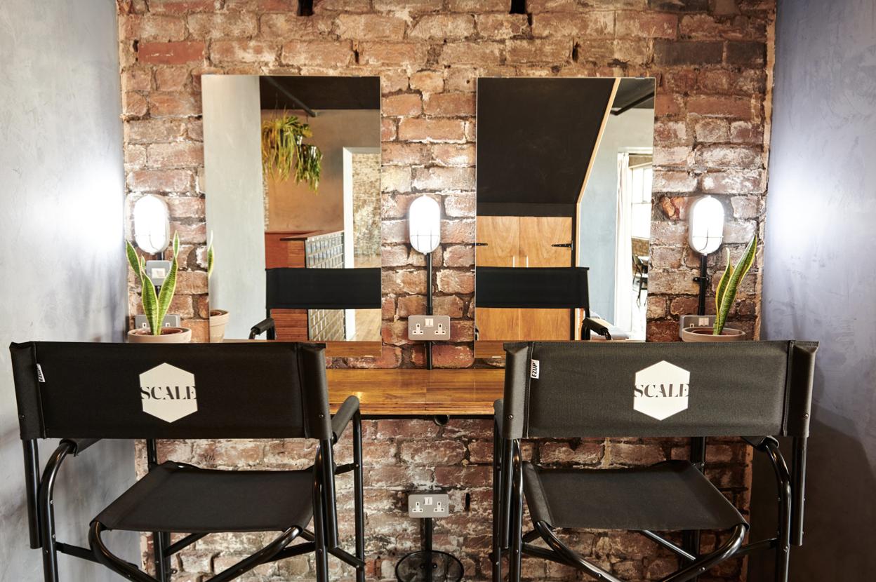 A photo studio with exposed brick walls, director chairs, and vanity mirrors with lights at Scale, Liverpool.