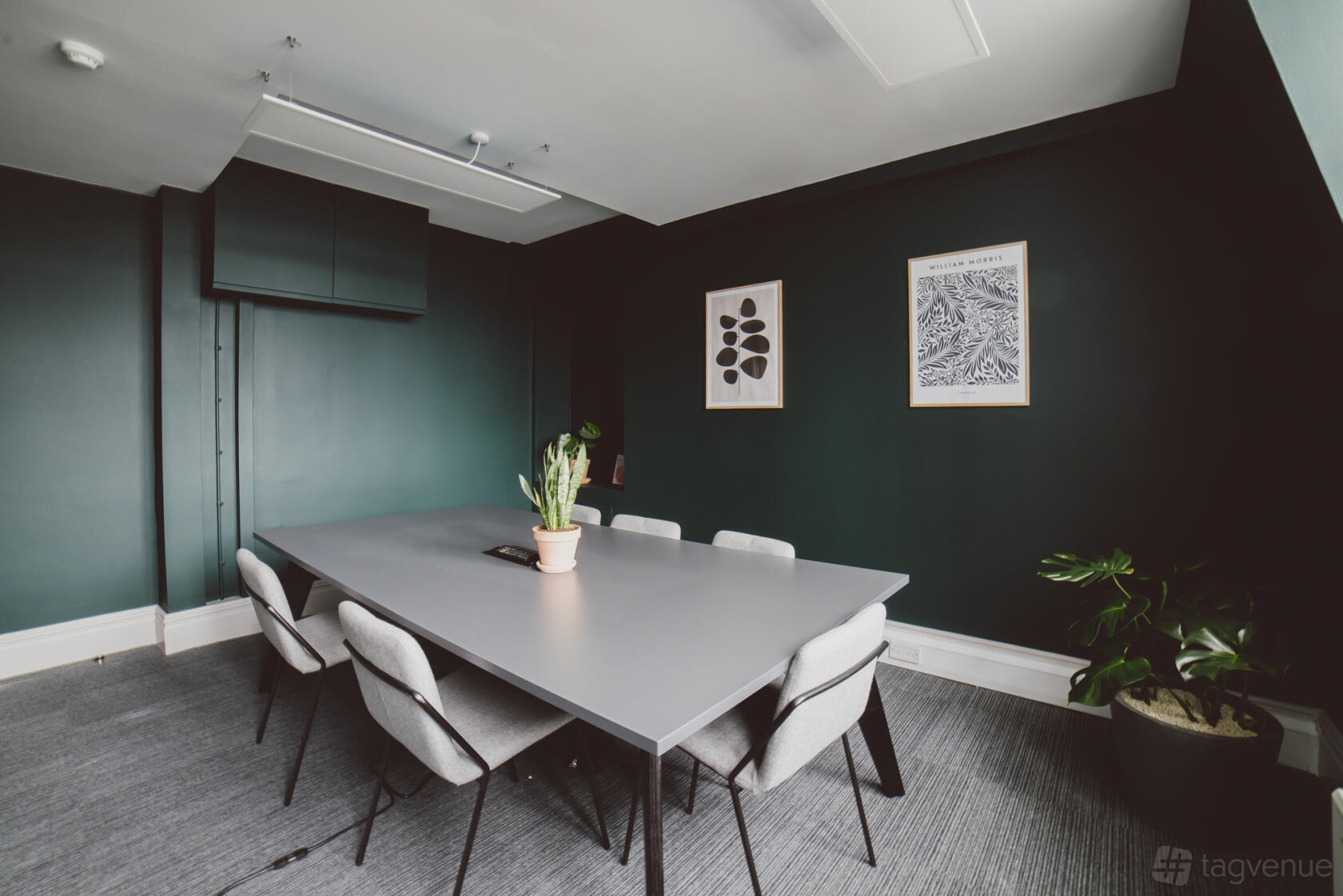 A meeting room with a gray conference table, upholstered chairs, dark green walls, and potted plants at Clement Rooms by Spacemade.