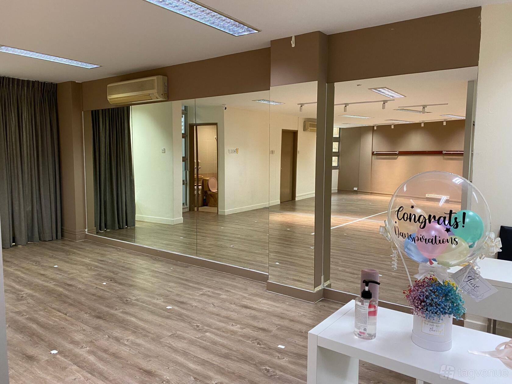 A dance studio with full-length mirrors, wood flooring, and ceiling lights at Danspirations Studio 2.