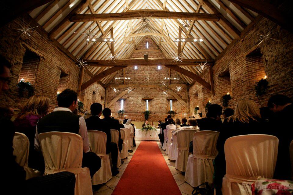 A barn venue with exposed brick walls, timber beams, and rows of chairs with white covers at Elms Barn.