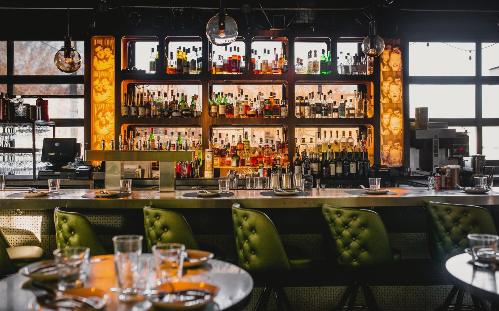 A restaurant lounge with tufted green barstools, backlit liquor shelves, and pendant lighting at Root Down.