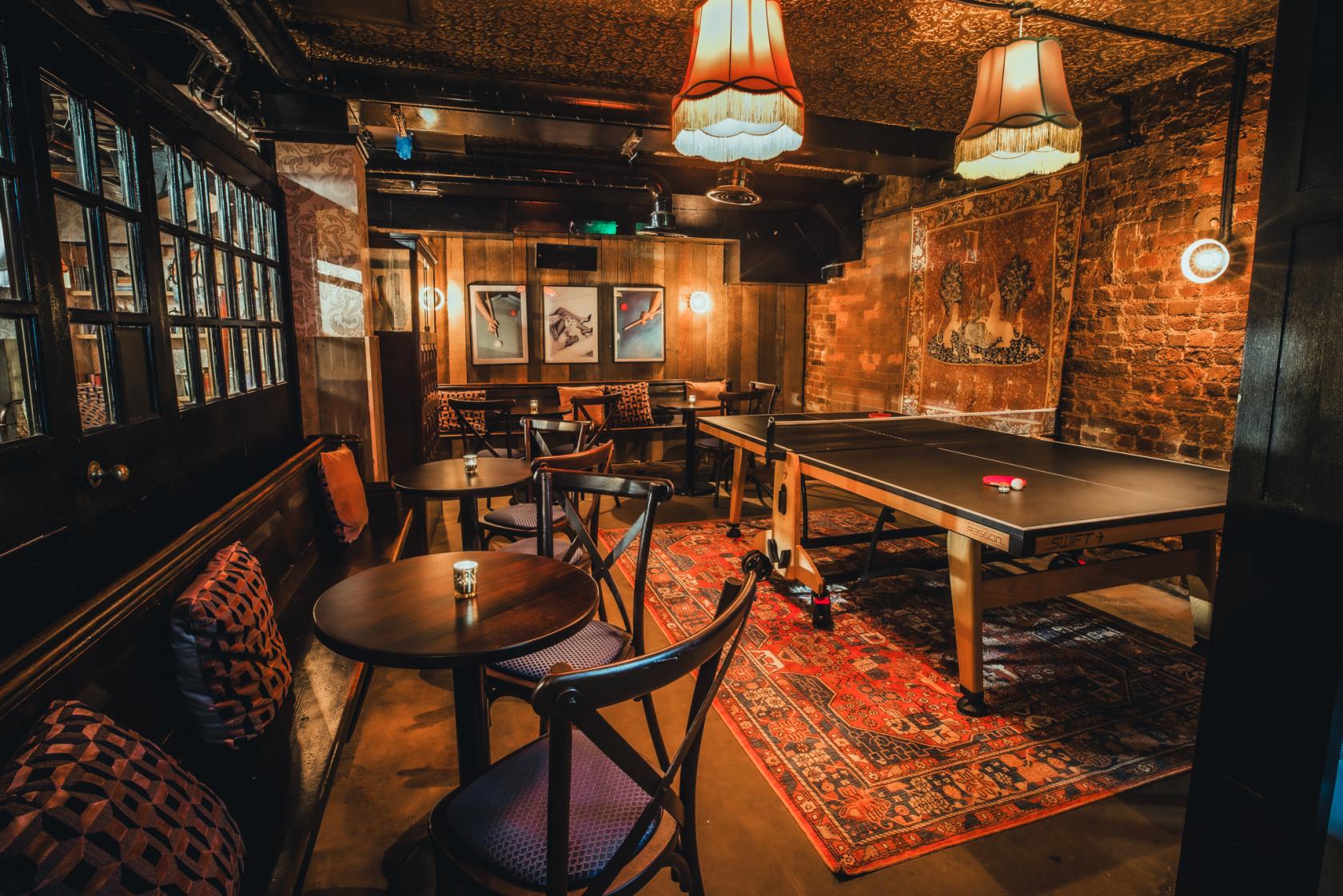 An event space in a cocktail bar with a ping pong table, exposed brick walls, and vintage pendant lights at The Cocktail Club Old Street.