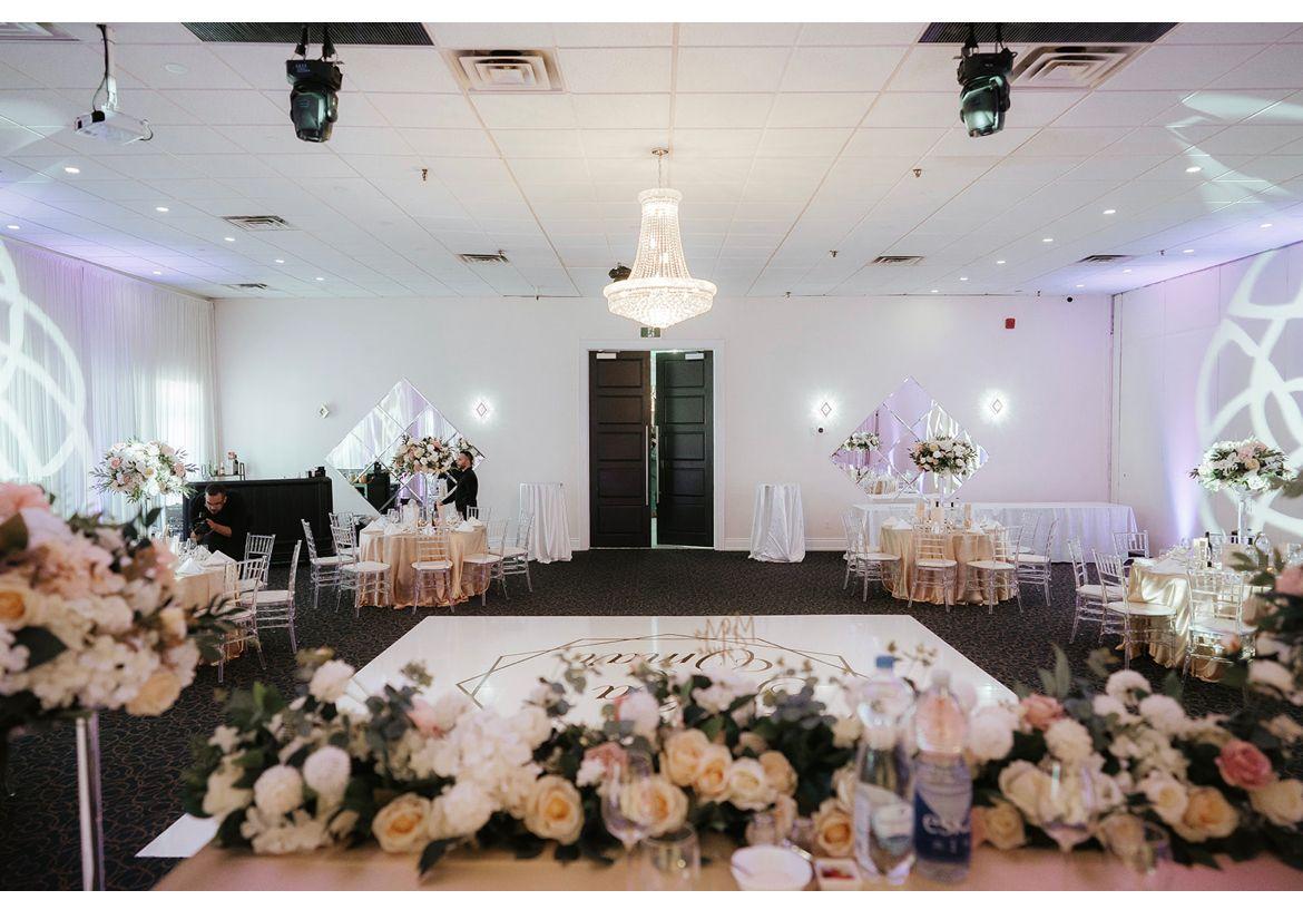 A banqueting hall with a large dance floor, round tables with white linens, and floral centerpieces at Casa Ricca.