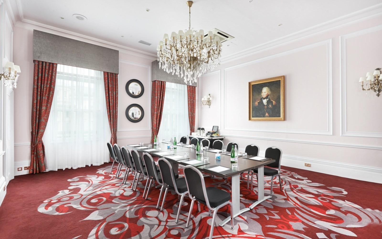 A meeting room with chandeliers, ornate red carpet, and a long conference table at Clermont Charing Cross.