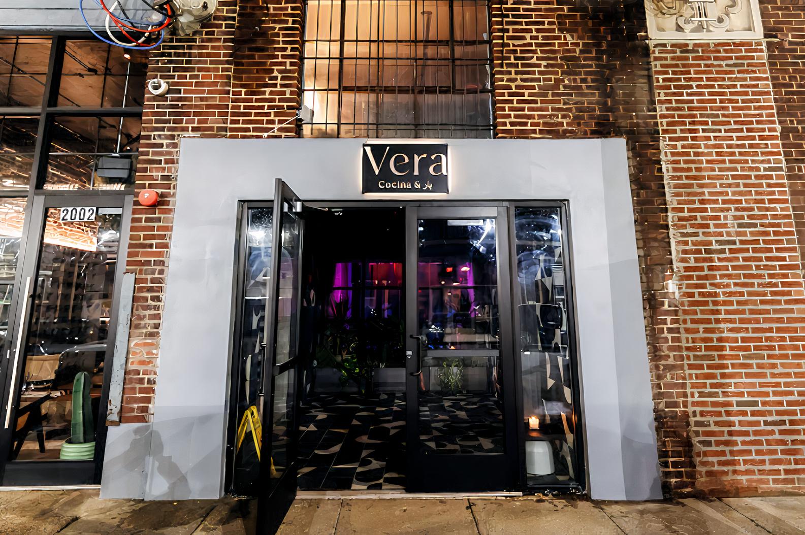 A restaurant entrance with glass doors, brick exterior, and illuminated sign at Vera Cocina and Bar.
