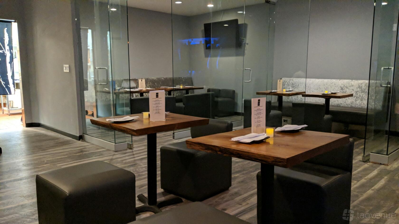 A restaurant with wooden tables, black cushioned seating, glass walls, and minimalist decor at Aura Cinema.