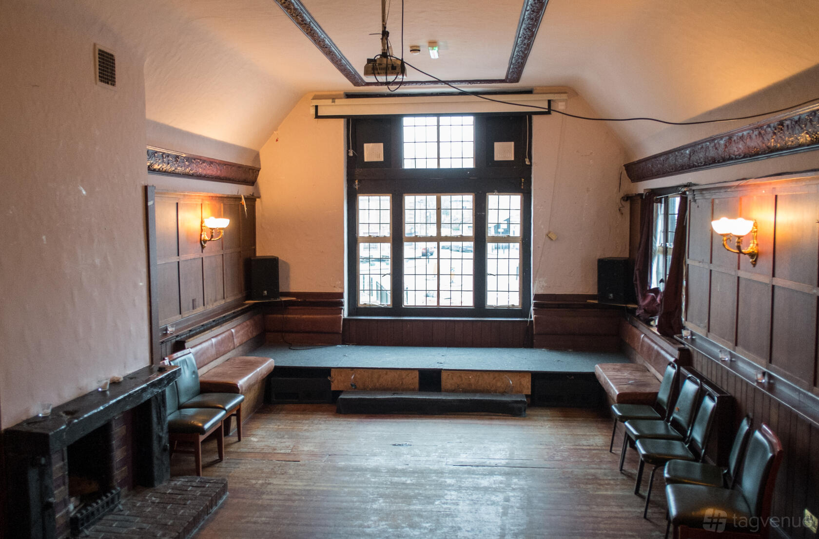 A function room with wood-paneled walls, a raised platform, fireplace, and large windows at The Old Nun's Head.
