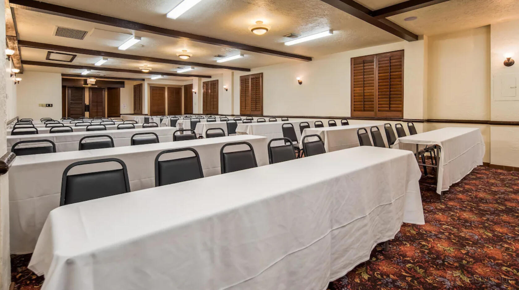 A meeting room with long tables draped in white linens and rows of black chairs at Best Western Plus Hacienda Hotel Old Town.