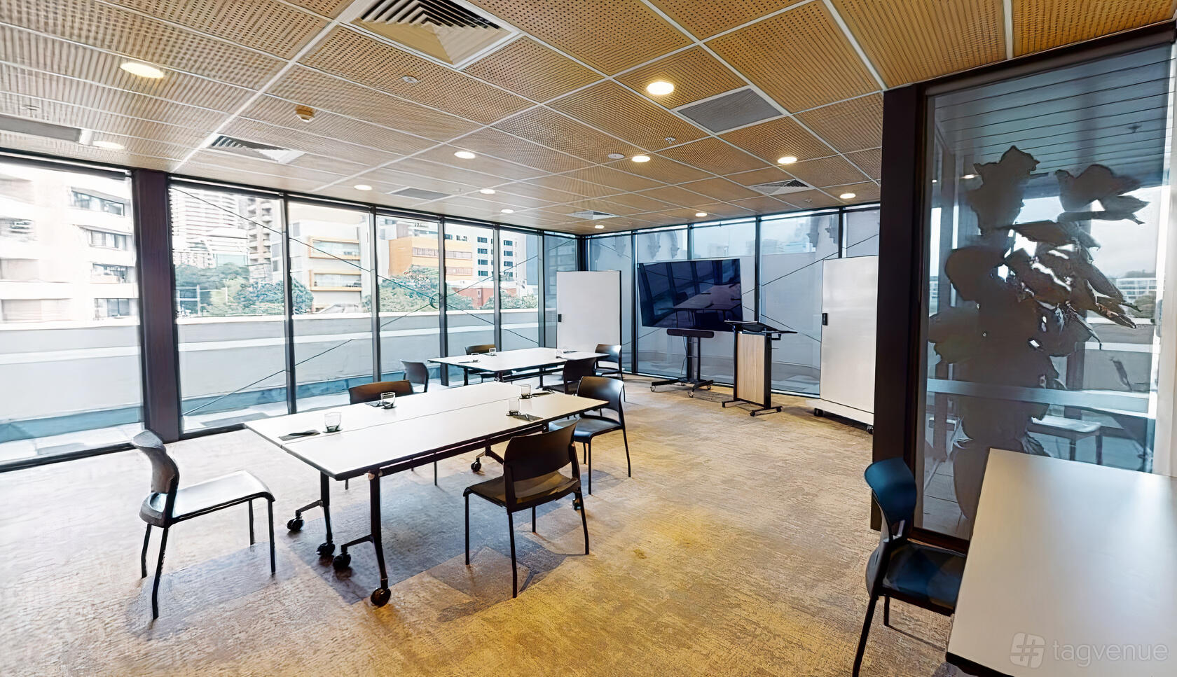 A function room with floor-to-ceiling windows, movable tables, chairs, and presentation screens at Hub Hyde Park.