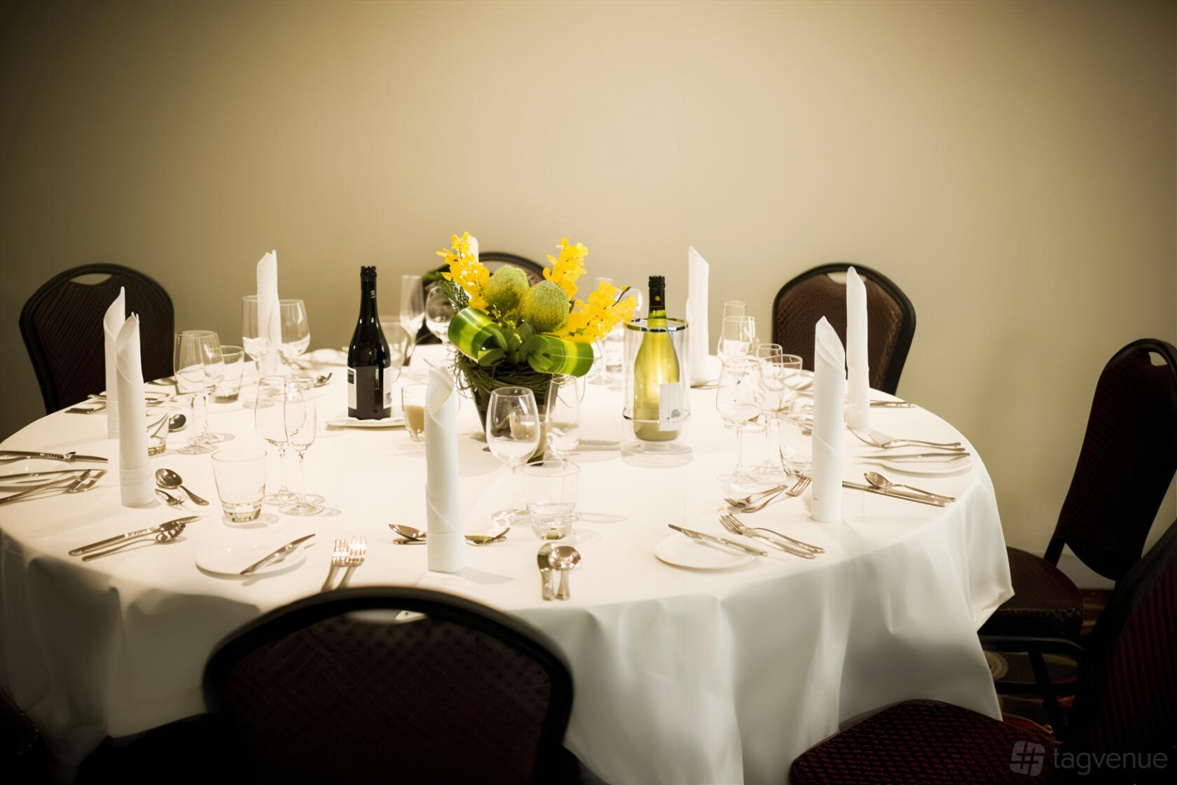 An event space with a round table set with white linens, floral centerpiece, and glassware at Mantra Melbourne Airport.