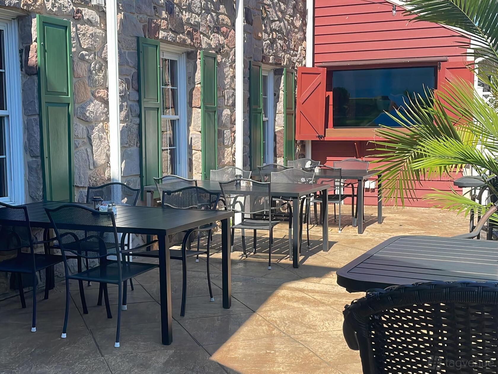 A hotel terrace with black metal tables and chairs, stone walls, and green window shutters at The Buck Hotel.