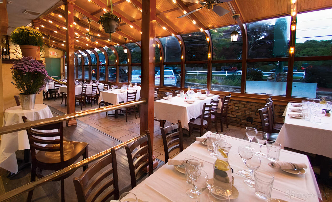 An event space in a restaurant with glass walls, string lighting, and tables set with white linens at Rocco's Restaurant & Bar.