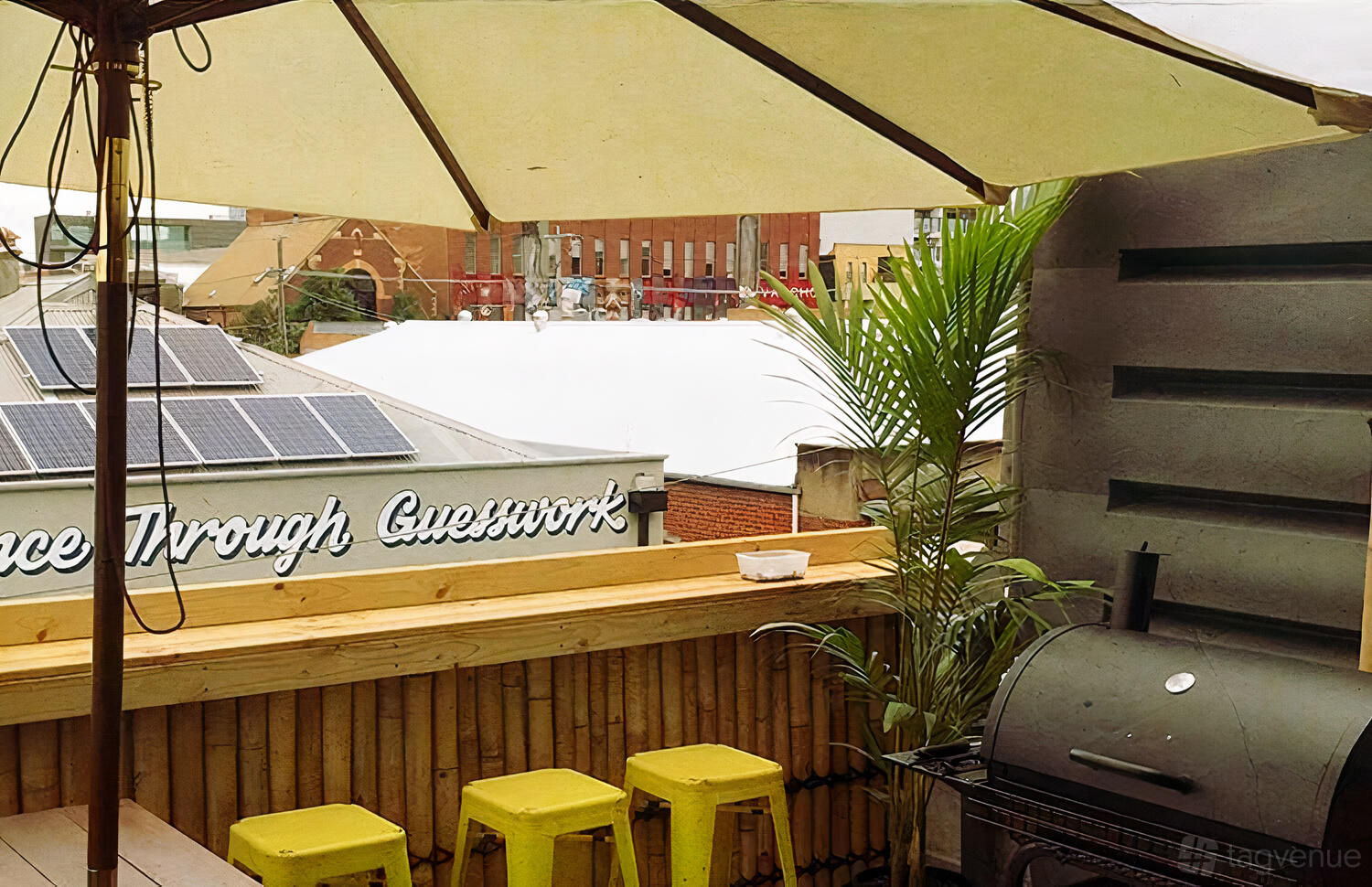 An outdoor event space with yellow stools, a barbecue grill, wooden railing, and large umbrella at Easey's.