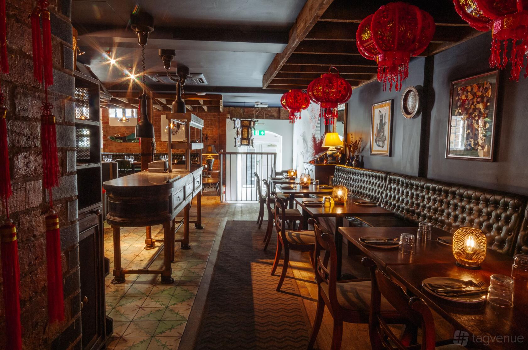 A restaurant with tufted leather banquettes, wooden tables, and red lanterns at The Last Talisman.