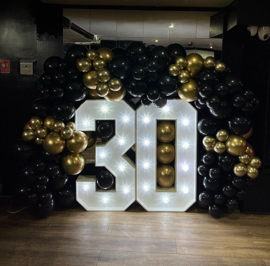 A bar with a large illuminated '30' sign surrounded by black and gold balloons at Basement 144.