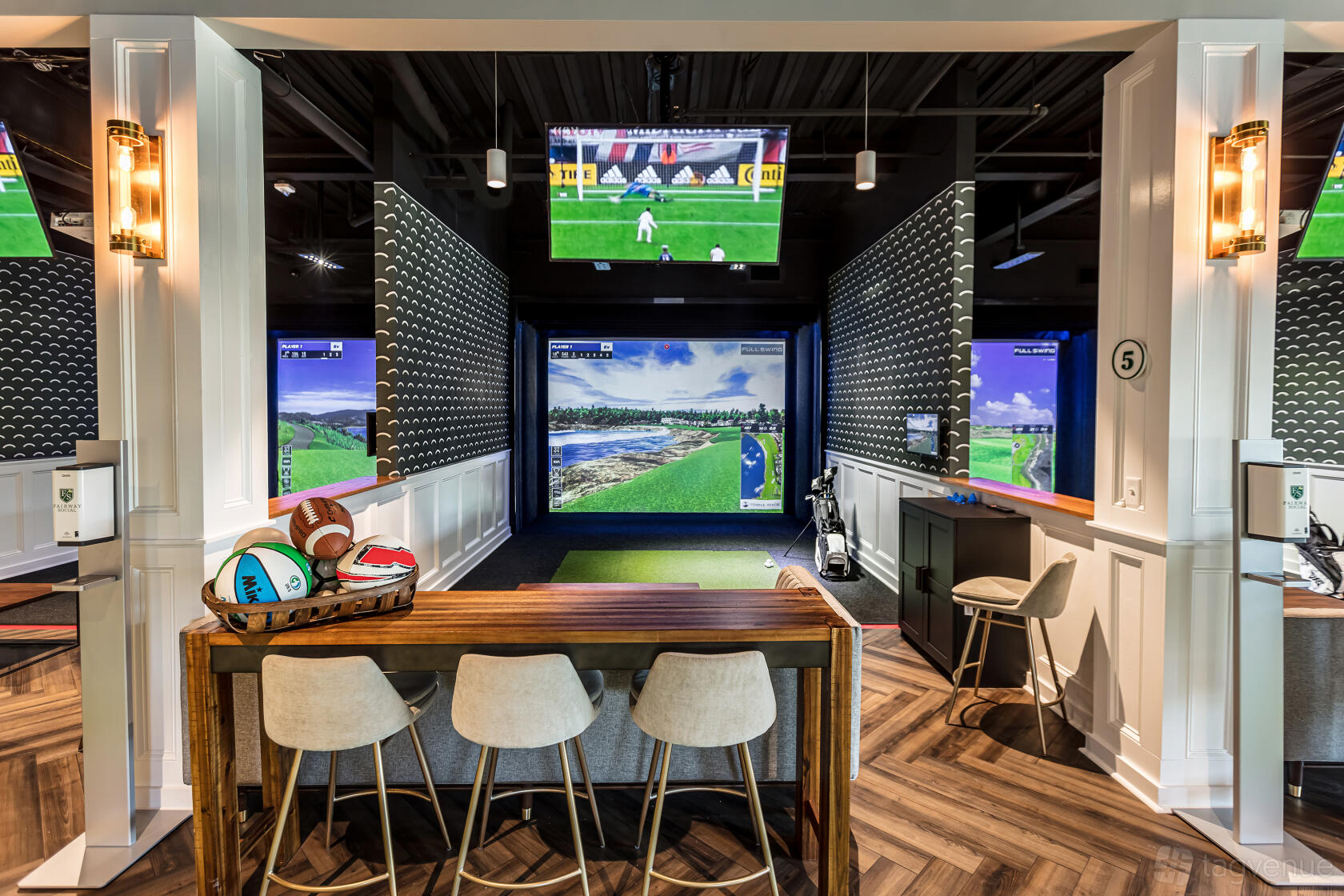 A restaurant lounge with golf simulators, wood floors, and a counter with stools at FAIRWAY SOCIAL.