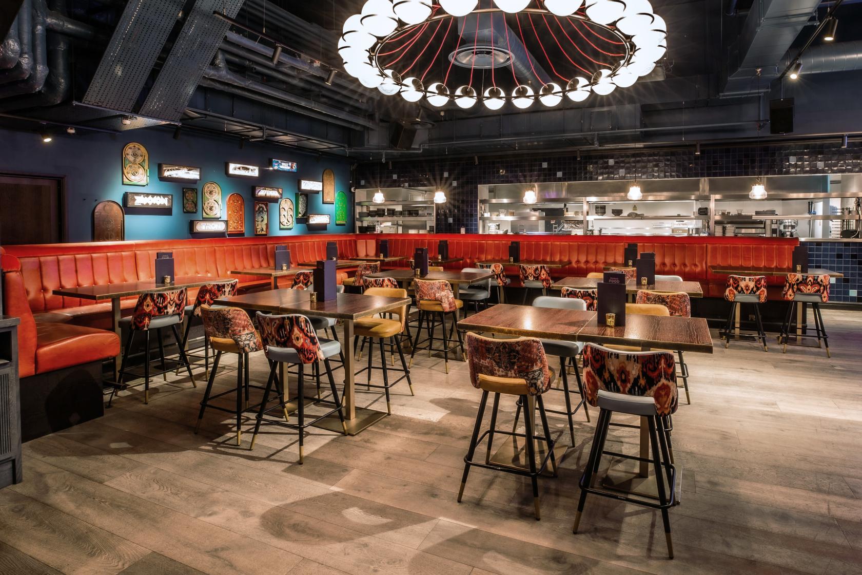 An event venue with patterned upholstered chairs, red banquettes, and a large circular chandelier at Puttshack Bank.