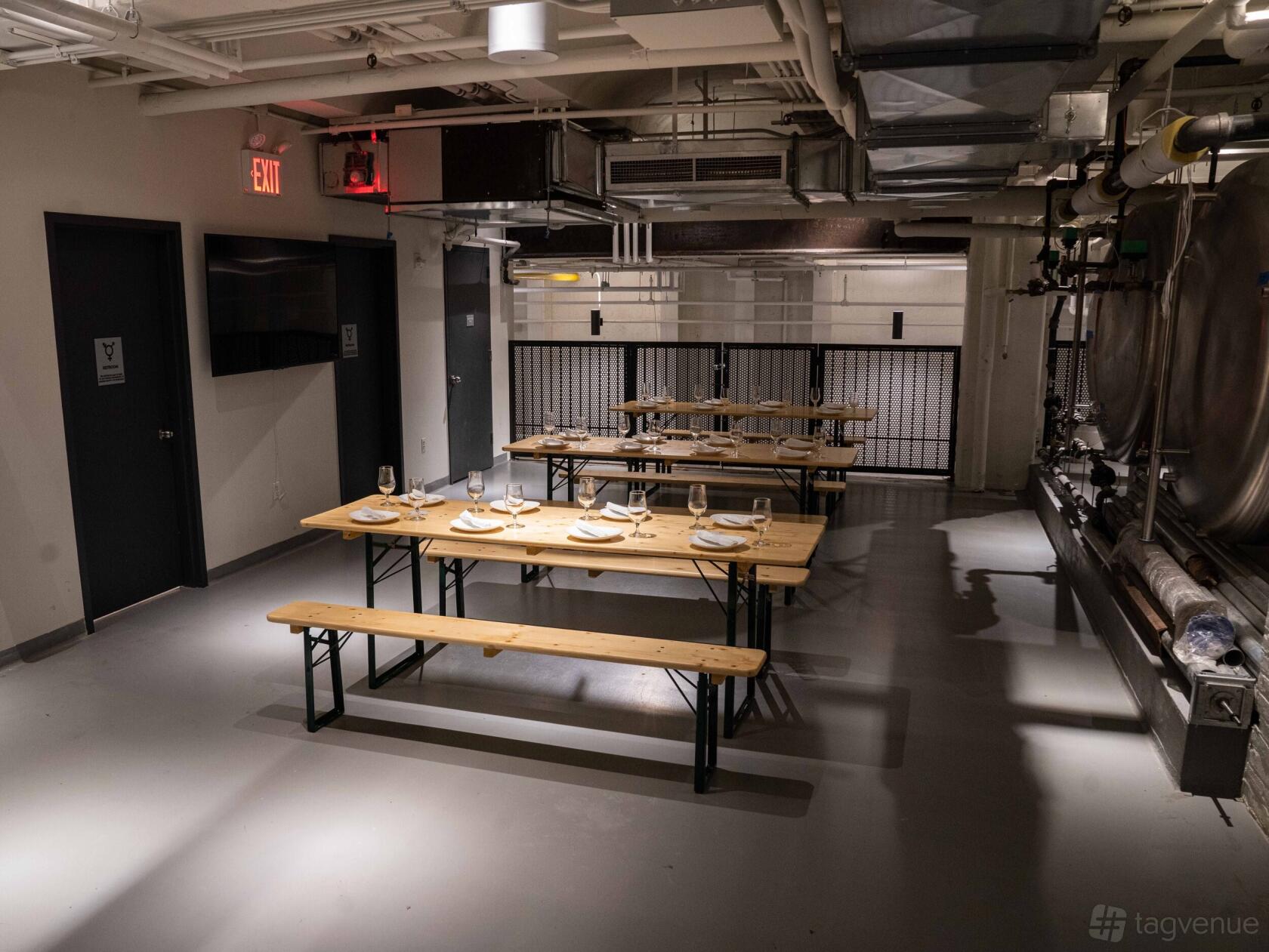 A brewery basement with long wooden tables, benches, and industrial steel tanks at Torch and Crown.