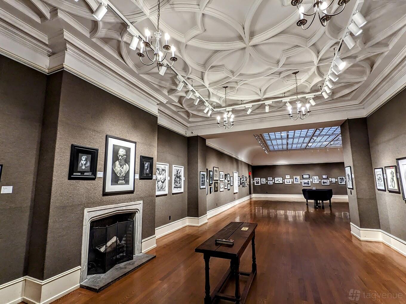 A gallery with framed artwork, a coffered ceiling with track lighting, and a grand piano at The Salmagundi Club.