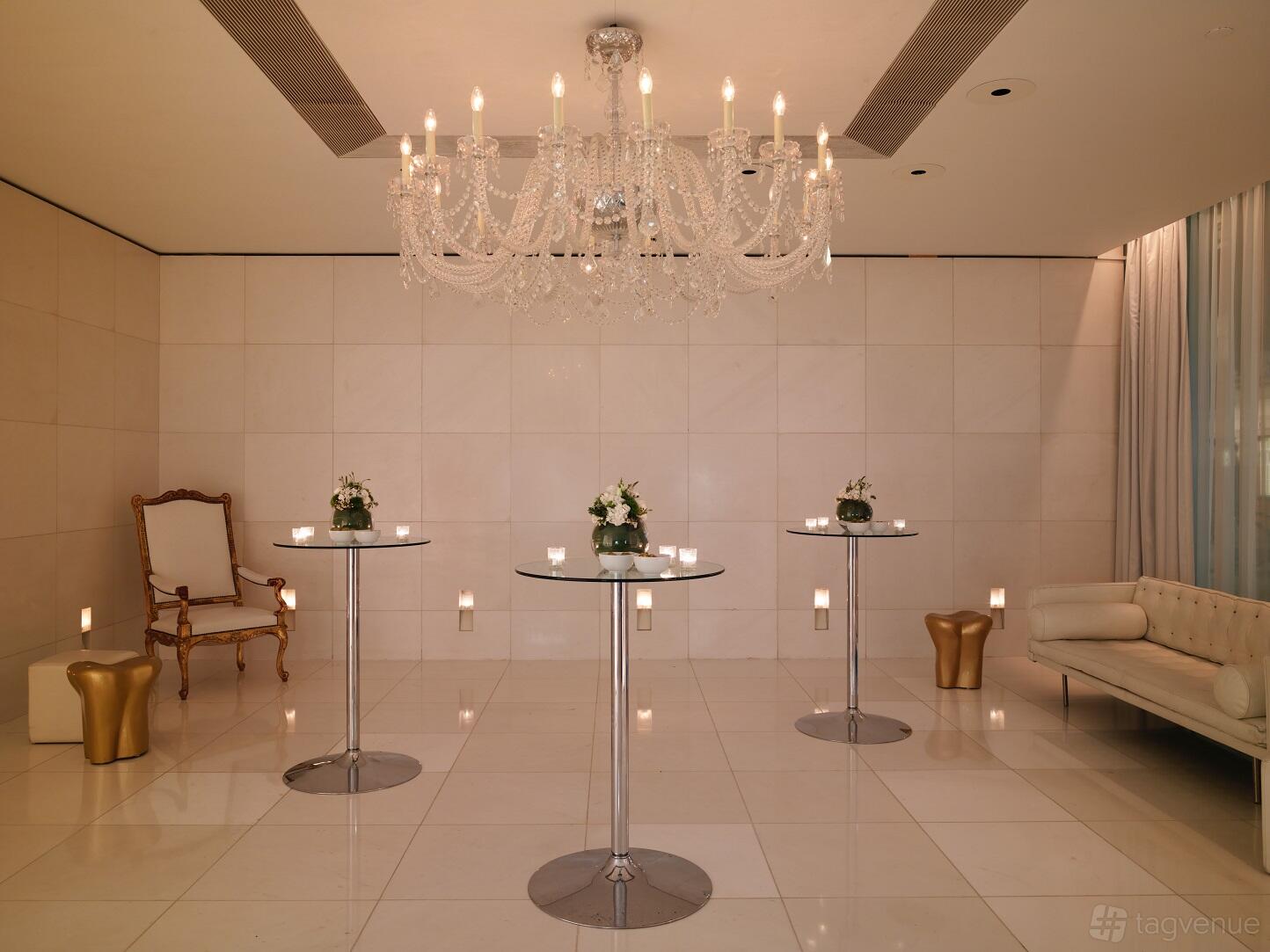An event space with a crystal chandelier, high tables with floral centerpieces, and white tiled floors at St Martins Lane London.
