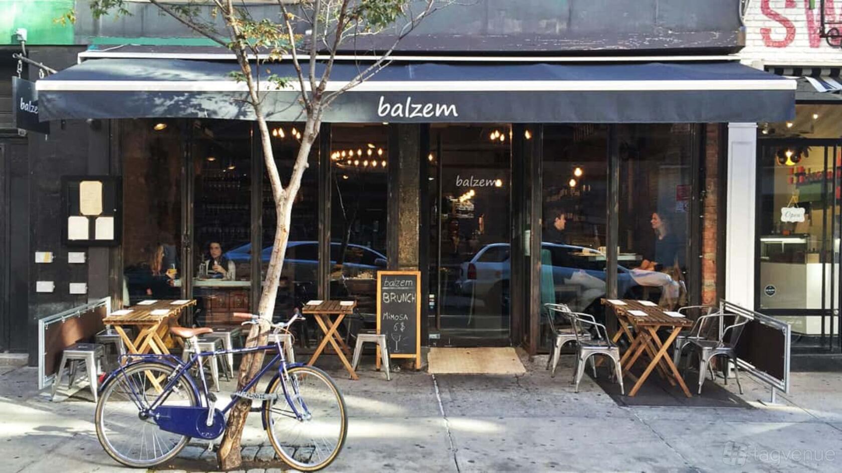 A restaurant with outdoor sidewalk seating, metal chairs, and a black awning at Balzem.