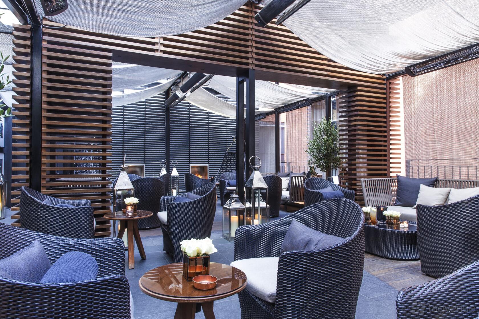 A hotel terrace with woven lounge chairs, sheer canopies, and wooden slat dividers at The May Fair Hotel.