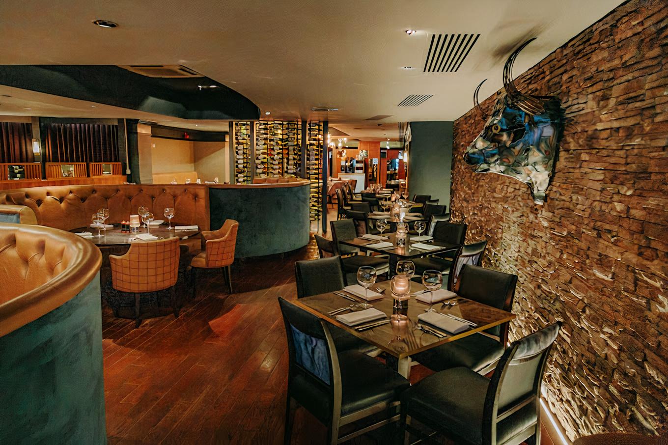 A restaurant with exposed stone walls, a decorative bull sculpture, wine display, and leather banquette seating at Bo'Vine Meats & Wines.