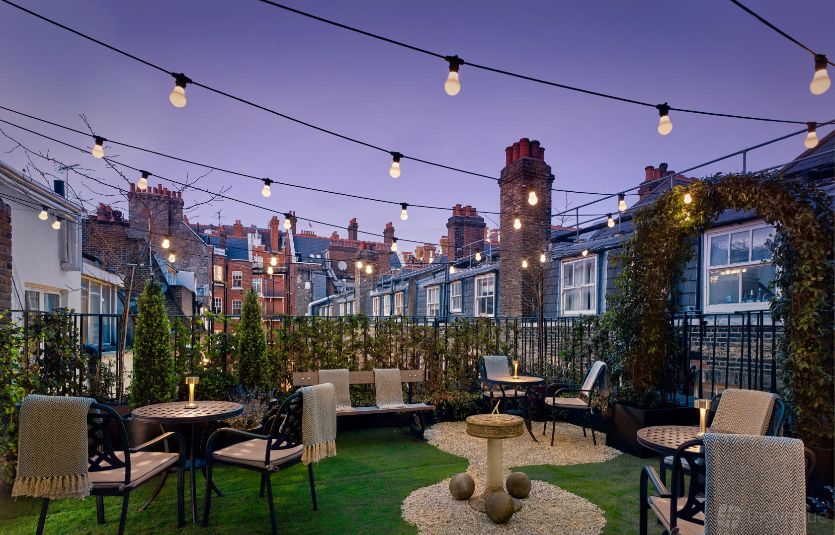A hotel terrace with string lights, outdoor seating, and greenery at The Residence at Holmes Hotel London.