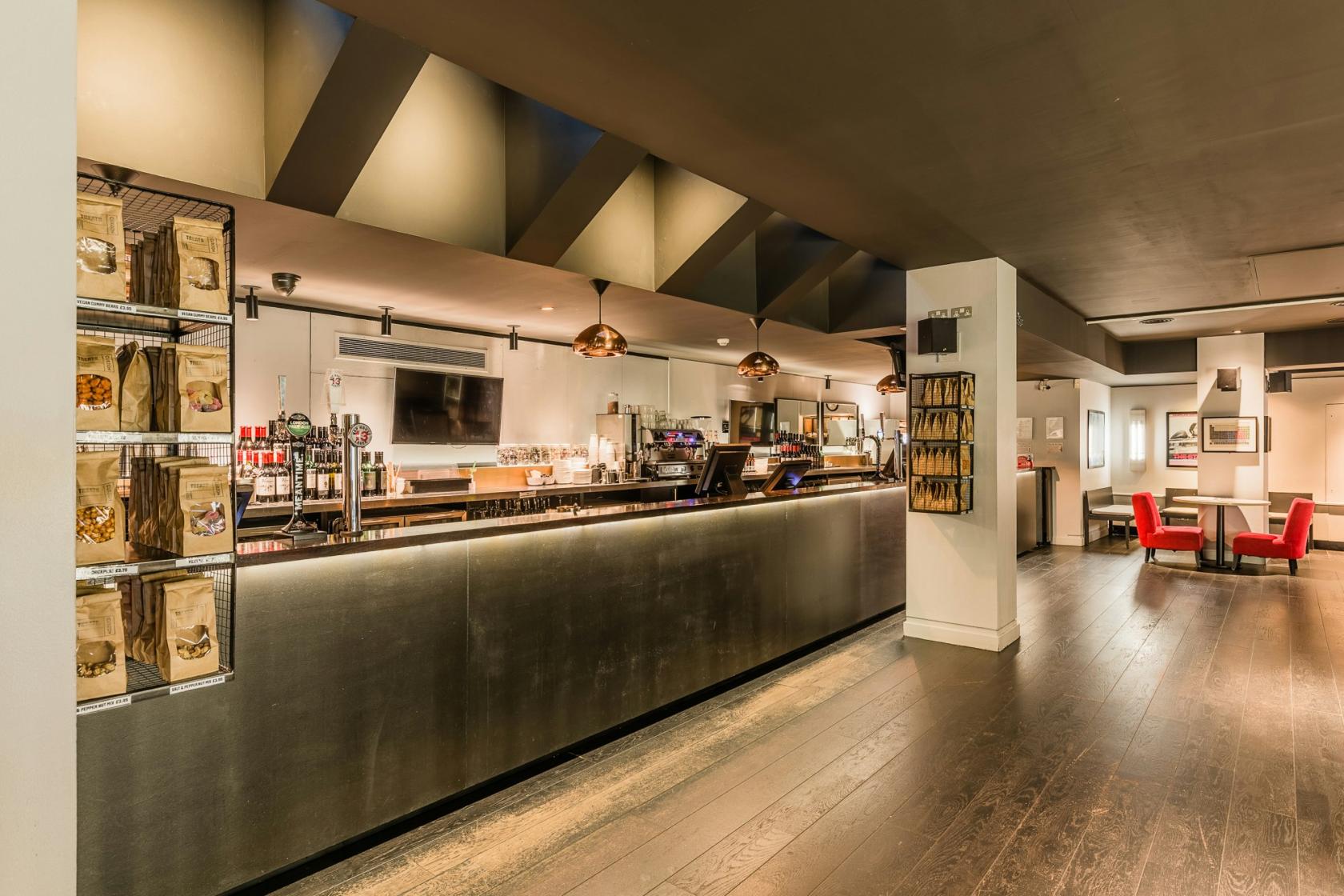 A cinema bar with a long metal counter, pendant lighting, and snack displays at Curzon Soho.